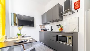 A modern kitchen with grey cabinets, a built-in microwave, and a flat-screen TV mounted on the wall. - Studio 2 - Gorgeous Studio in Earls Court (London)