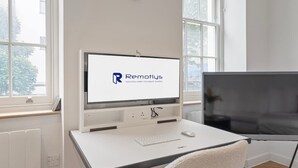 Un espacio de oficina moderno con un escritorio blanco, un monitor de computadora mostrando un logotipo, un teclado, un ratón y un televisor de pantalla plana grande.