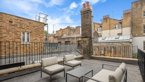 Terraza en la azotea con mobiliario exterior, una chimenea de piedra y edificios de ladrillo circundantes.