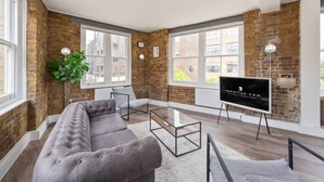 A modern living room with a grey sofa, a glass coffee table, and a flat-screen TV on an easel. - Spacious Bright Oasis in Old Street (London)