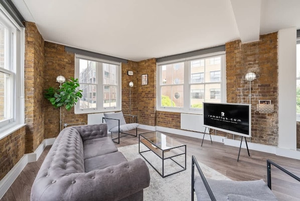 A modern living room with a grey sofa, a glass coffee table, and a flat-screen TV on an easel.