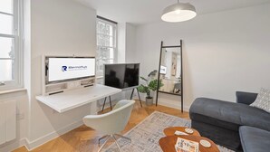 Un salon moderne avec un téléviseur à écran plat, un bureau avec un ordinateur, un canapé gris et une grande fenêtre.