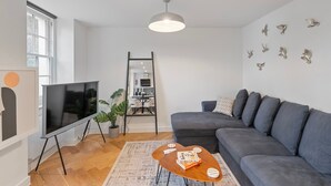 Un salon moderne avec un canapé gris, un téléviseur à écran plat, une table basse en bois et un luminaire au plafond.