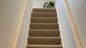 Una escalera con peldaños cubiertos de moqueta beige y paredes blancas.