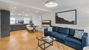 Una sala moderna con un sofá azul, una mesa de centro de cristal y un comedor con sillas blancas.