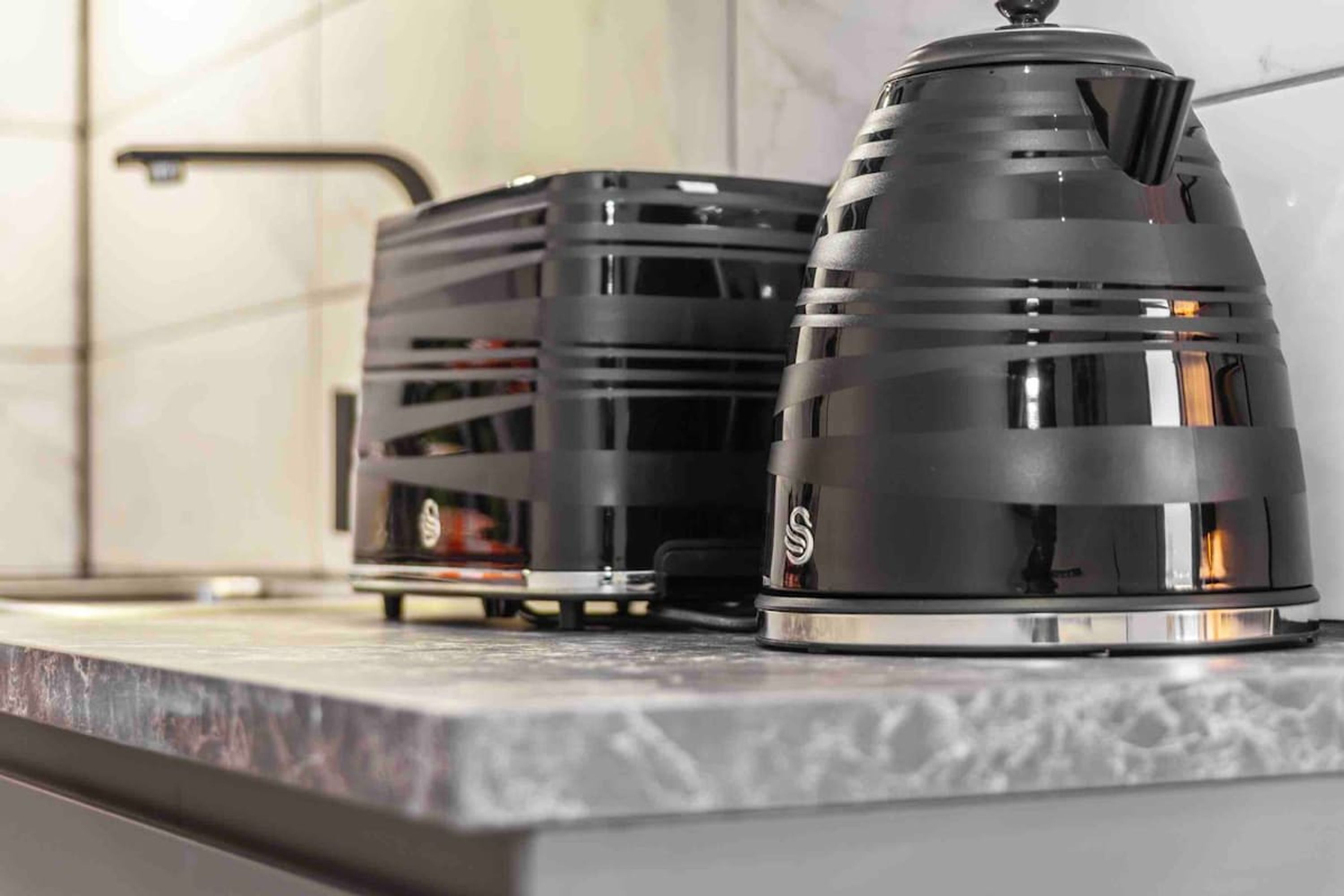 A kitchen counter with two black kettles and a coffee maker.