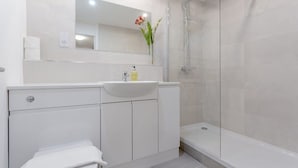 Ein modernes Badezimmer mit Waschbecken, Spiegel und Dusche, alles in Weiß.
