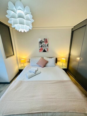 A hotel room with a large bed, two bedside lamps, a wall art piece, and a unique ceiling light fixture. - Kensington Gardens 2 Bedroom Flat With a Balcony (London)