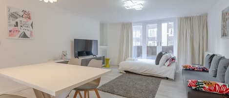 A modern, well-lit room with a dining table, sofa, and a bed.