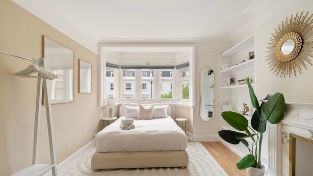 Un dormitorio con una cama grande, un tocador blanco, un espejo y una planta en maceta.