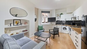 Un espacio habitable funcional con sofá, una mesita, lavadora, kitchenette y un espejo grande.