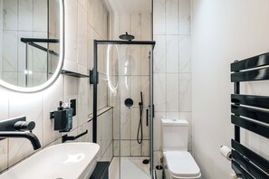 Et moderne badeværelse med en glasafskærmet brusekabine, en hvid vask og et toilet.