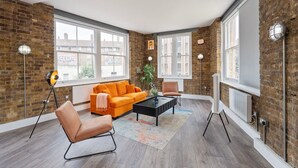 Ein modernes Wohnzimmer mit Backsteinwand, großen Fenstern, einer Couch, einem Couchtisch und einem Sessel.