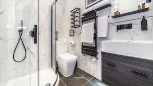 Une salle de bain moderne avec une douche à l’italienne en verre, des toilettes blanches, un meuble-lavabo en bois foncé et un pare-baignoire en marbre.