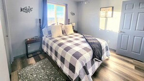 Ein Schlafzimmer mit einem Bett, einem Nachttisch, einem Fenster mit Vorhängen, einem Deckenventilator und einer Tür.