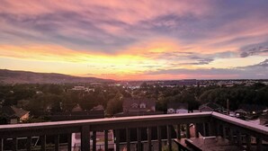 Sonnenuntergangblick von einem Balkon mit Blick auf ein Wohngebiet, Häuser und eine hügelige Landschaft.