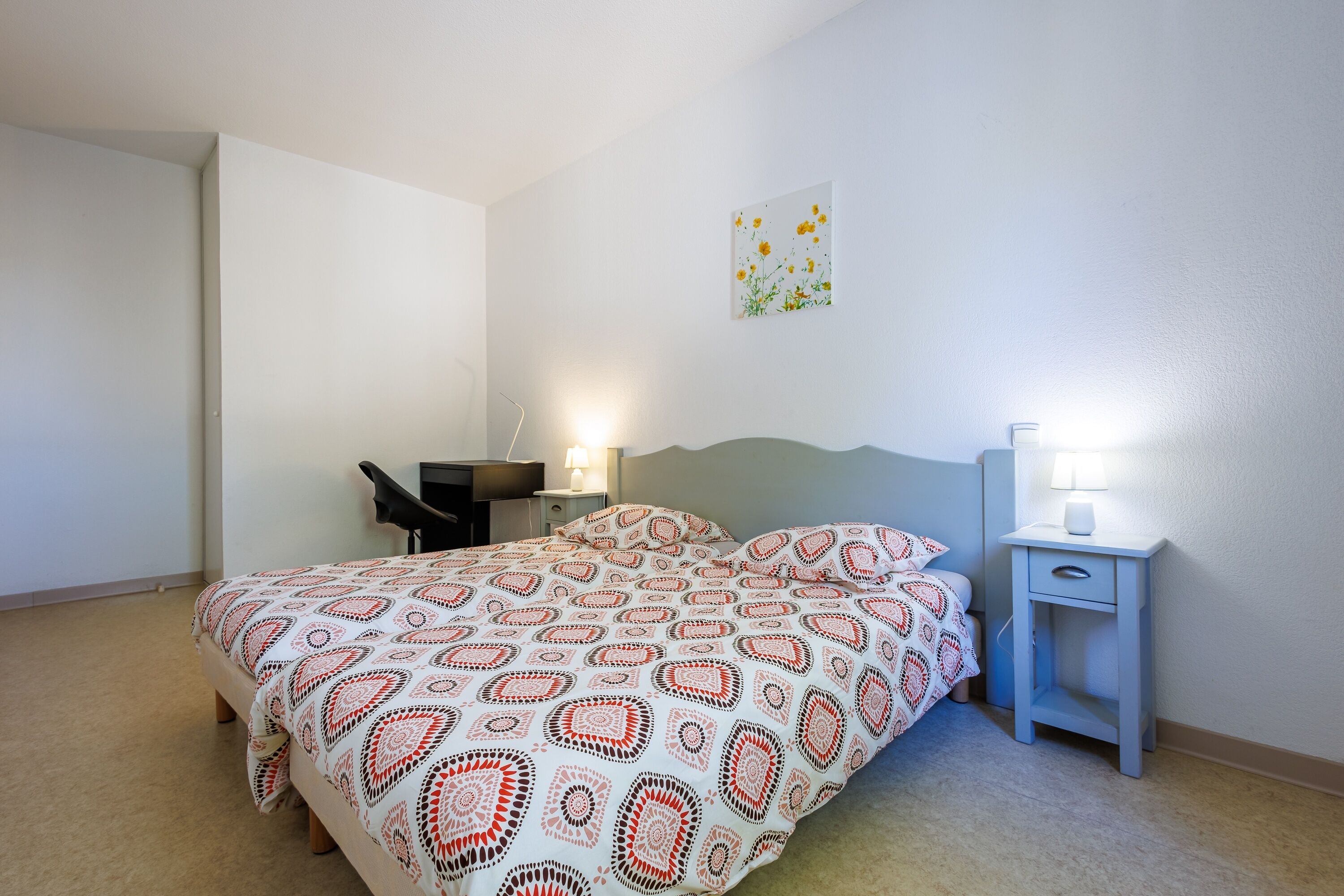 Een slaapkamer met een bed, nachtkastjes, een bureau en een wandlamp.