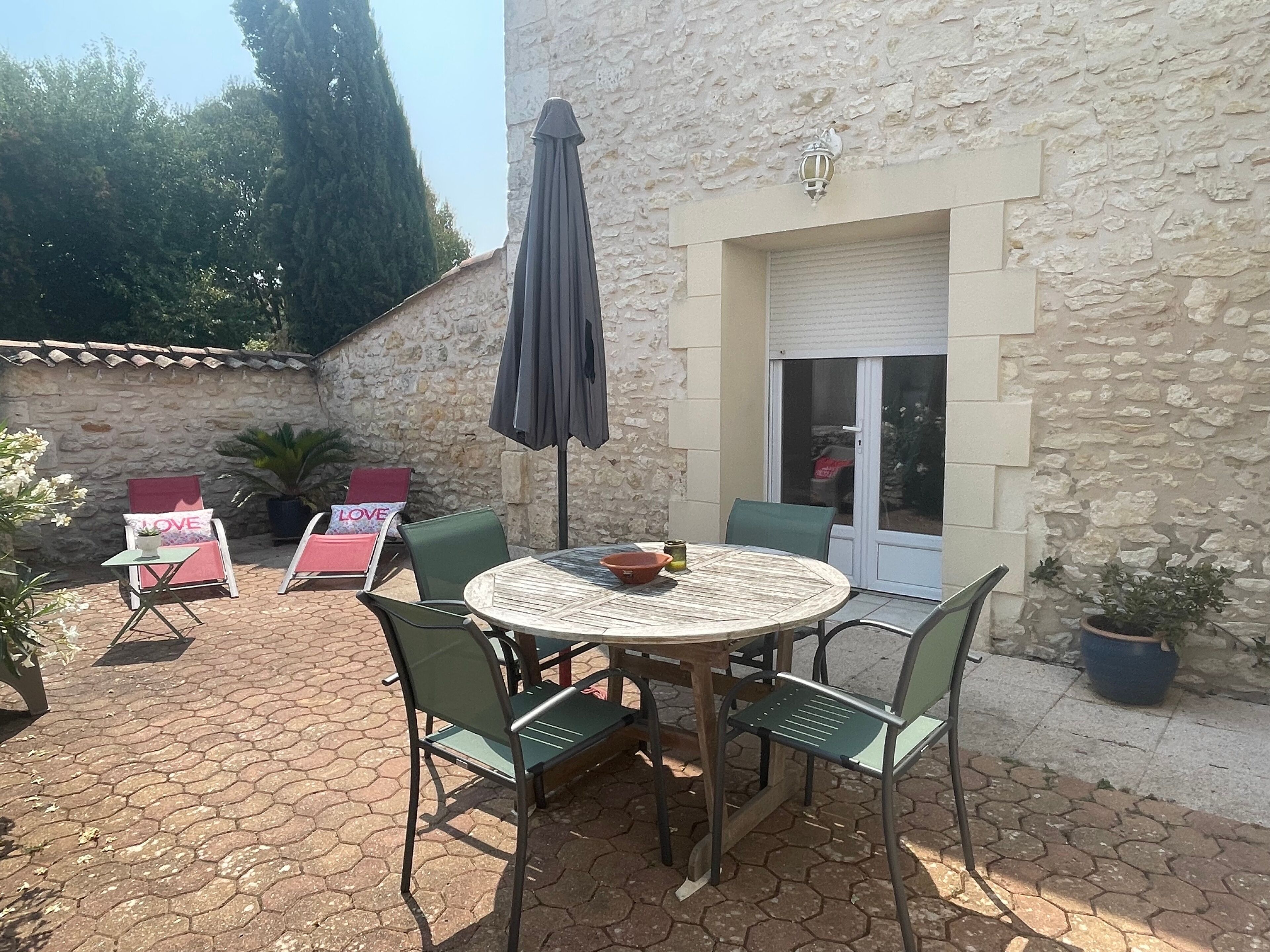 A patio with a round table and chairs, a potted plant, and a stone wall.