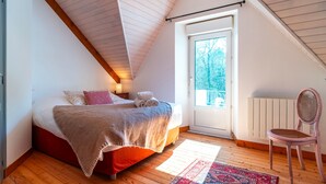 A bedroom with a sloped ceiling, a bed with a blanket, a chair, and a view through a door. - Ti an dour, entre terre et mer (Crac'h)