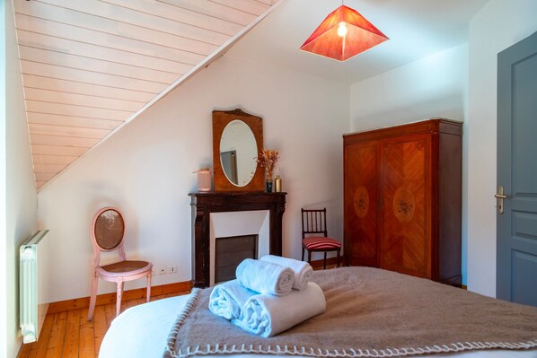 A bedroom with a sloped ceiling, a fireplace, a wooden wardrobe, a mirror, and a bed with rolled towels. - Ti an dour, entre terre et mer (Crac'h)