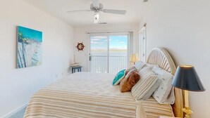 A bedroom with a bed, a ceiling fan, a nightstand, a lamp, a painting, and a view of the outdoors. - Charming 4-bedroom house with WiFi and AC in tranquil Ocean Pines (Ocean Pines)