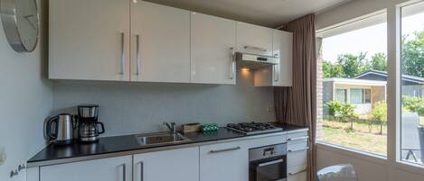 A modern kitchen with white cabinets, a stainless steel sink, a gas stove, and a coffee maker. There is a window with a view of a house and greenery outside.
