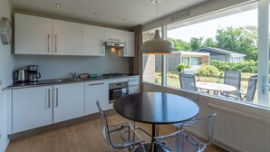 Cozinha moderna com armários brancos, fogão a gás e área de jantar com mesa redonda e cadeiras.