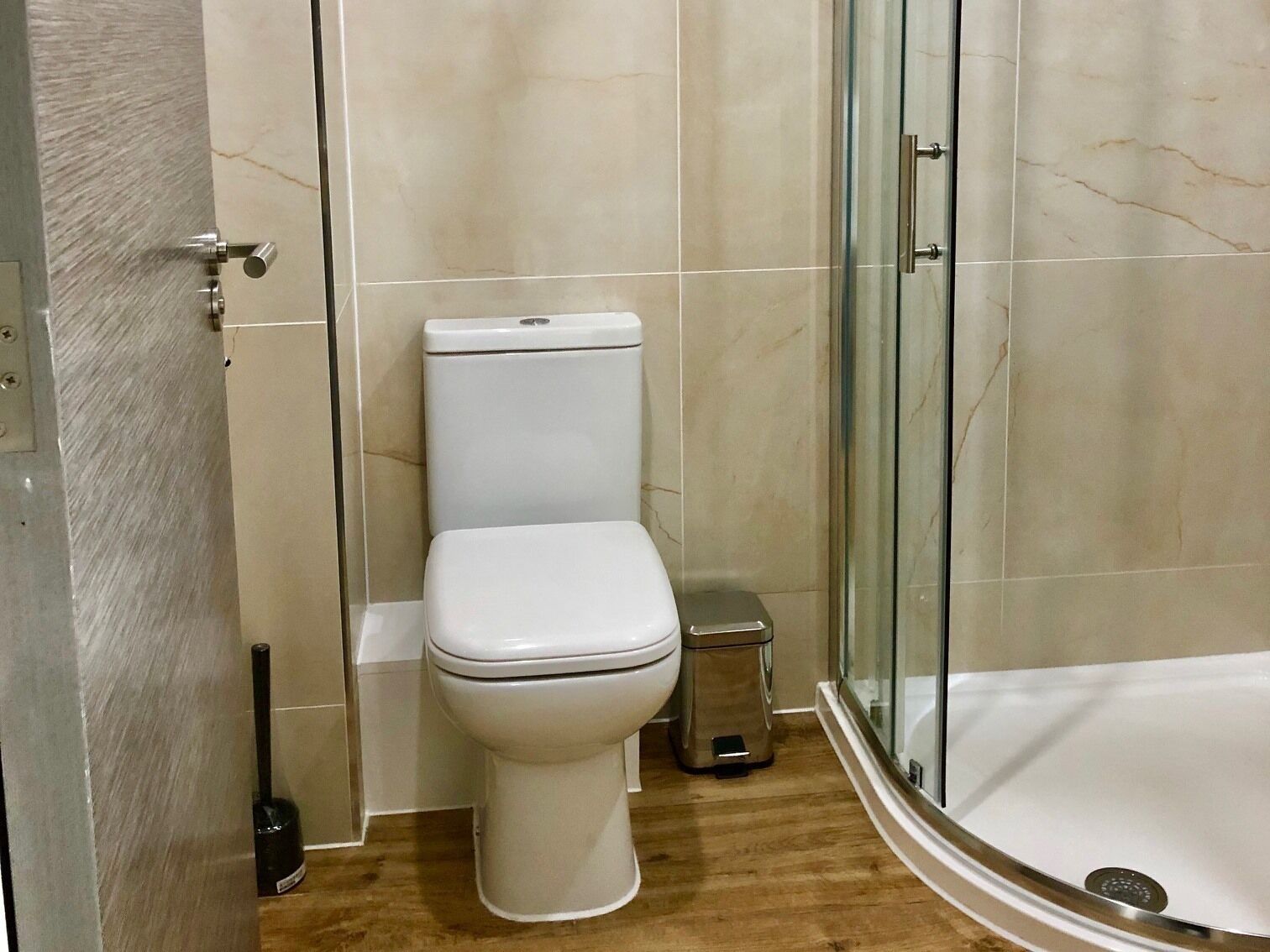 Uma casa de banho com sanita, um caixote de lixo e zona de duche separada por vidro.
