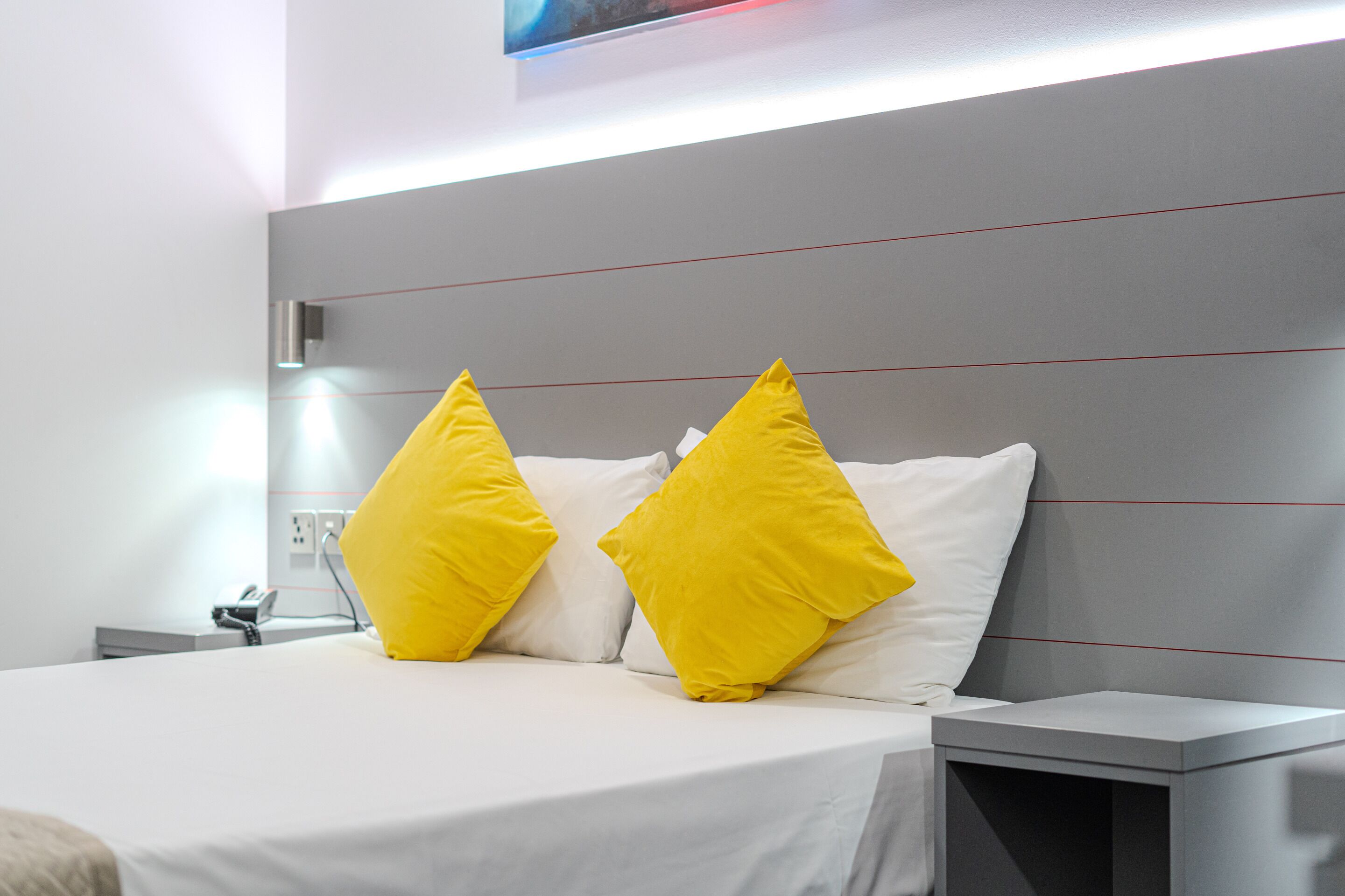Een moderne hotelkamer met een groot bed, twee heldergele kussens, een nachtkastje en een bijzettafeltje.