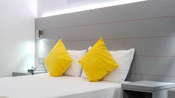 Een moderne hotelkamer met een groot bed, twee heldergele kussens, een nachtkastje en een bijzettafeltje.