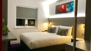 A modern hotel room with a large bed, bedside tables, a window with a view, and a painting on the wall.