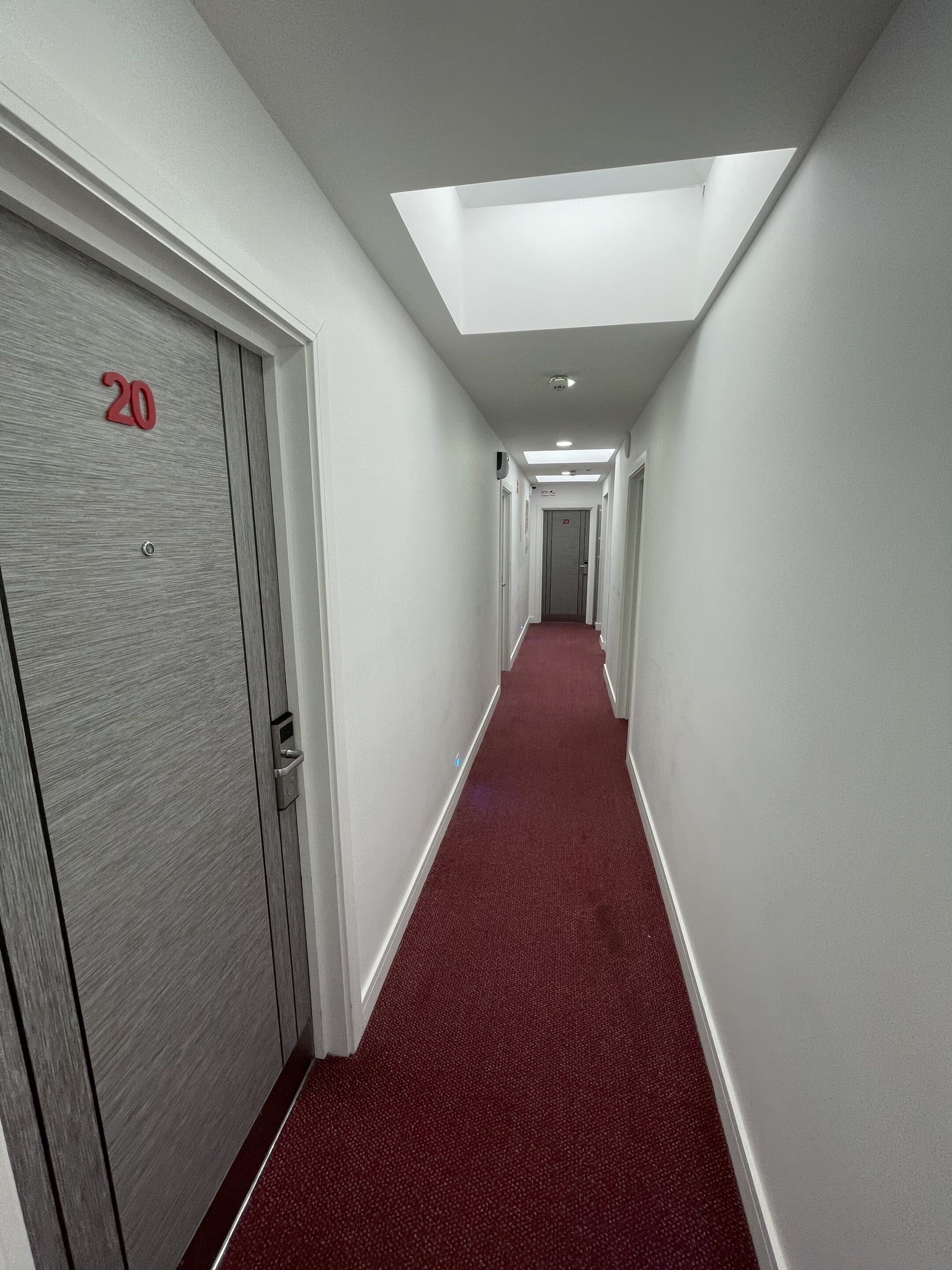 Un couloir avec un tapis rouge, des murs blancs et des portes numérotées 20 et 21.
