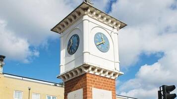 A clock tower with two faces, a cross on top, and a plaque with text.
