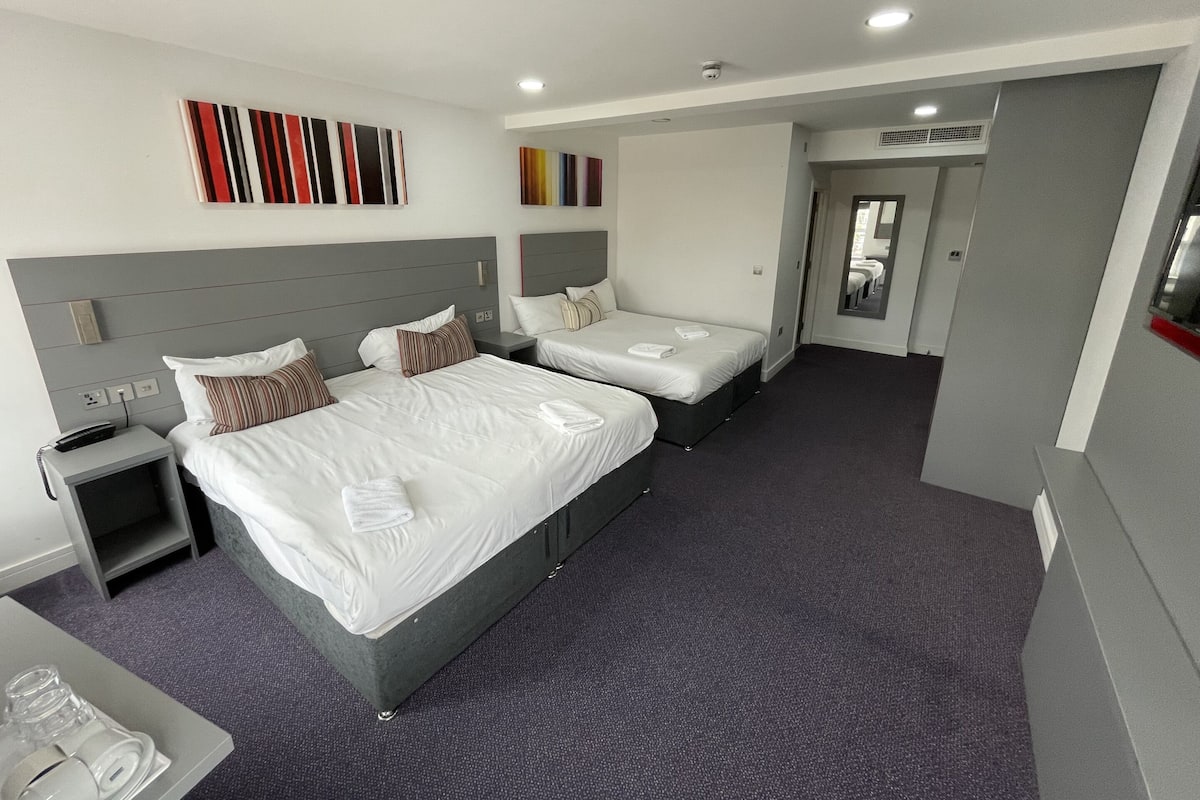 A hotel room with two beds, a desk, and a bathroom visible through an open door.