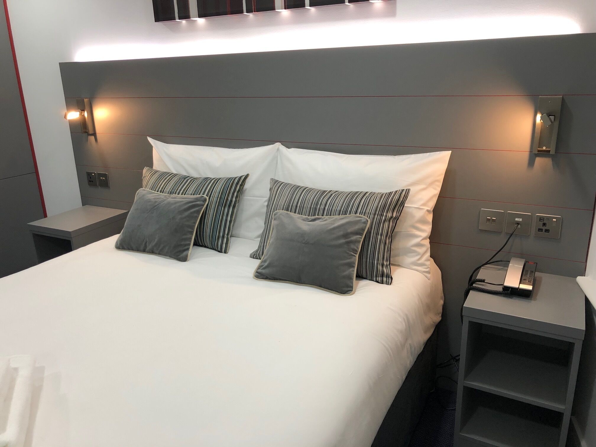 Una habitación de hotel moderna con una cama grande, dos mesitas de noche y un teléfono integrado.