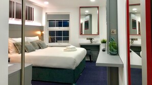 Una habitación de hotel moderna con cama, mesita de noche, escritorio y un espejo grande.