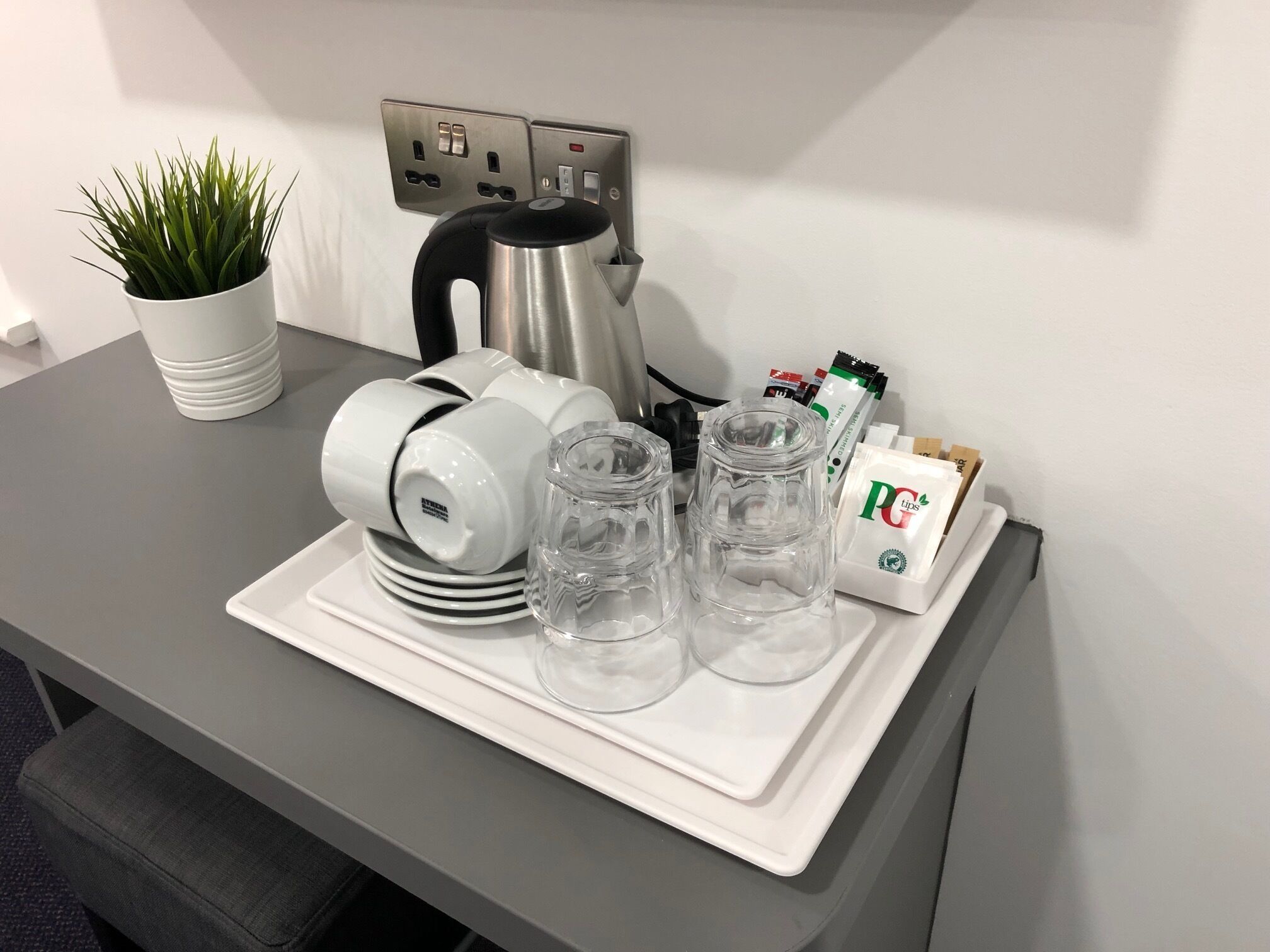 Eine Küchenarbeitsplatte mit Kaffeemaschine, Wasserkocher, einer Pflanze und einem Tablett mit Gläsern und einer Kaffeeweißer-Packung.