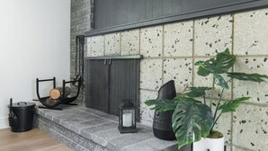 A stone fireplace with logs, a lantern, and a potted plant. - The Rodney House - Midcentury, Modern Sleeps 8 (Reno)