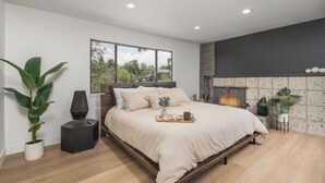 A modern bedroom with a large bed, a fireplace, and a view of the outdoors. - The Rodney House - Midcentury, Modern Sleeps 8 (Reno)