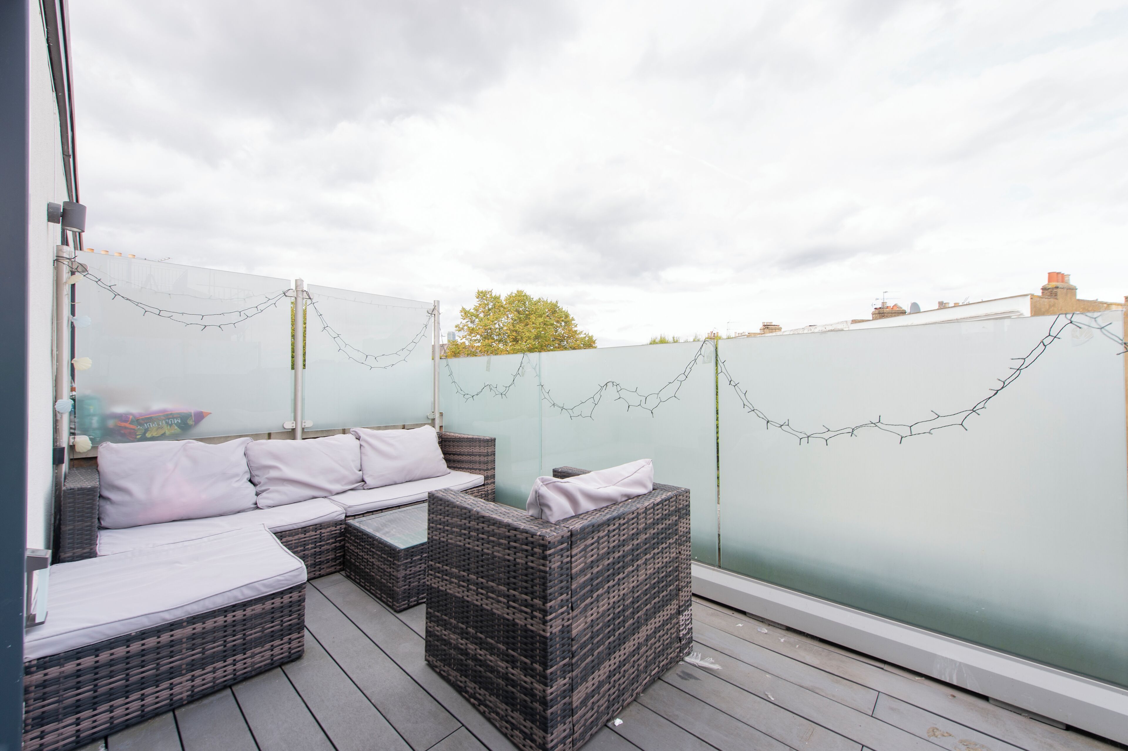 A rooftop patio with wicker furniture, a glass partition, and a chain-link fence.
