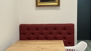 Ruokailutilassa on puinen pöytä, punaisella kankaalla päällystetty penkki ja valkoiset tuolit.