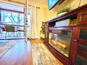 A living room with a fireplace, a television mounted on the wall, and a view through a glass door to an outdoor area with chairs and a table. - Lakeside Home in Reno (Reno)
