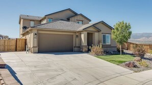 A two-story house with a garage, a well-maintained lawn, and a view of mountains in the background.