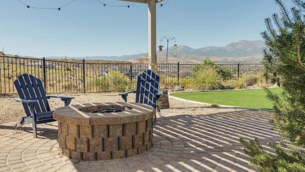 A patio area with two Adirondack chairs, a stone fire pit, and a view of mountains.