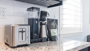 A kitchen with a toaster, a coffee maker, and a bag of coffee beans on a granite countertop.