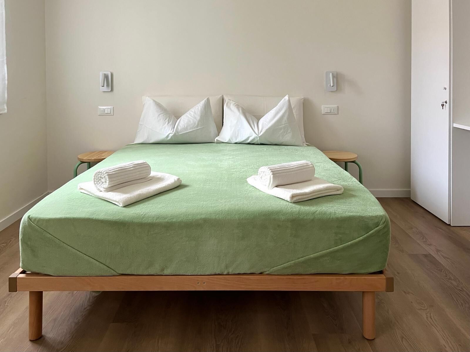 Una cama bien hecha con una colcha verde, dos almohadas blancas y dos toallas dobladas sobre la cama.