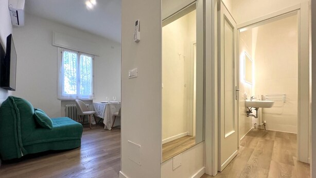 Un apartament modern amb un sofà verd, zona de menjador i un bany amb rentapel i mirall.