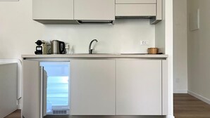 Una cuina moderna amb armaris blancs, un rentapesos integrat i una petita illa amb un frigorífic.