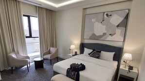 A hotel room with a large bed, two bedside tables, a chair, a small table, and a window with curtains. - BRAI HOTEL (Al Duwadimi)