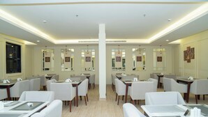 A modern hotel dining area with multiple tables and chairs, a central pillar, and artwork on the walls. - BRAI HOTEL (Al Duwadimi)
